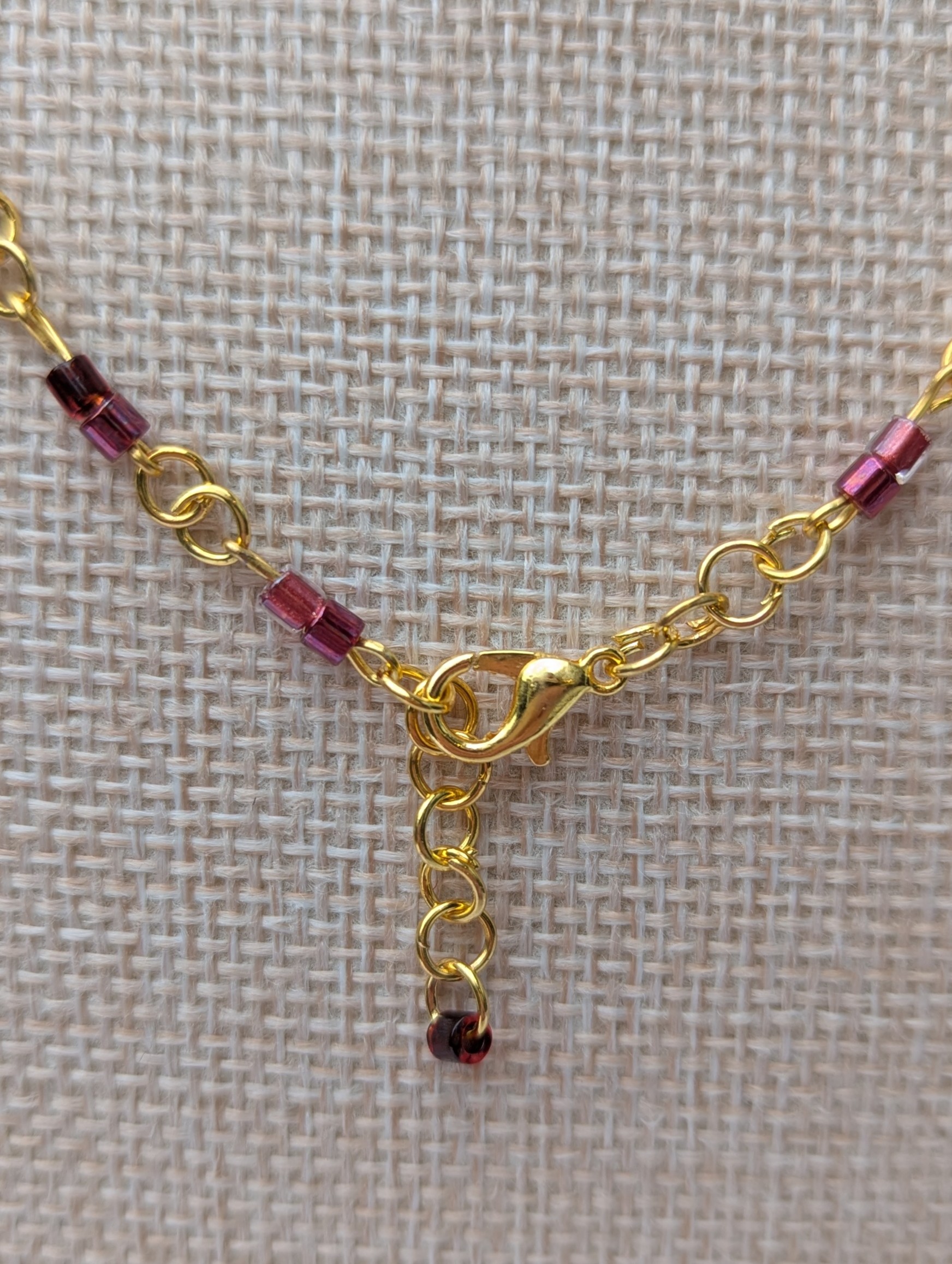 Handmade gold-toned double chain necklace with garnet, burgundy, and deep wine glass seed beads, featuring an ornate gold pendant and lobster clasp closure.