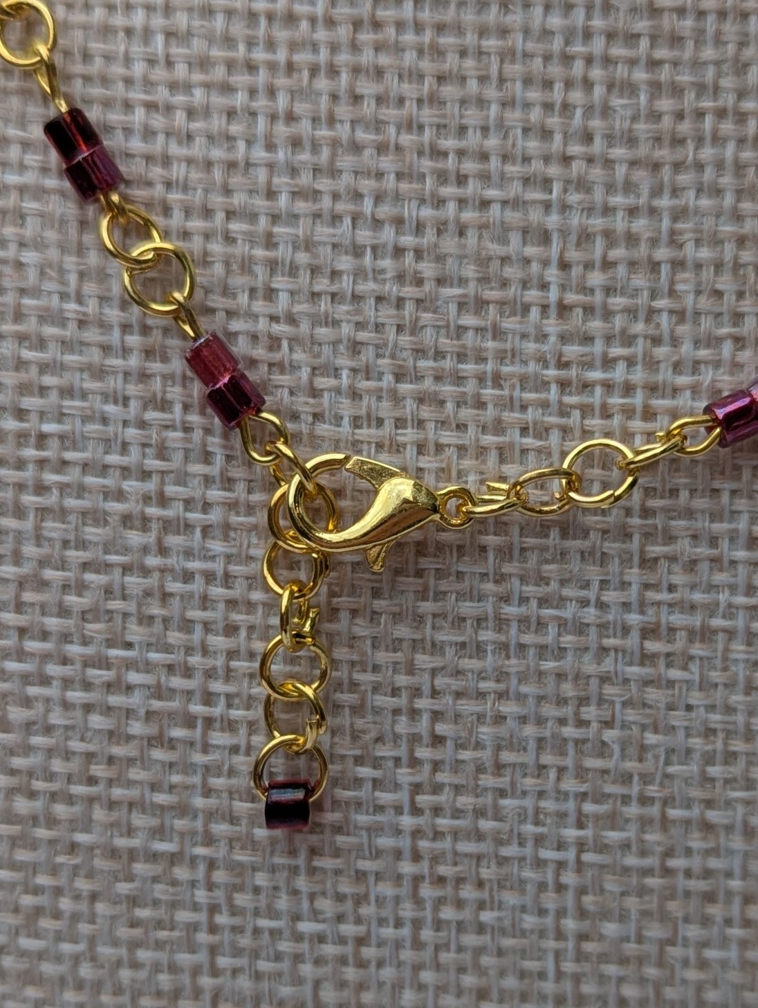 Handmade gold-toned double chain necklace with garnet, burgundy, and deep wine glass seed beads, featuring an ornate gold pendant and lobster clasp closure.