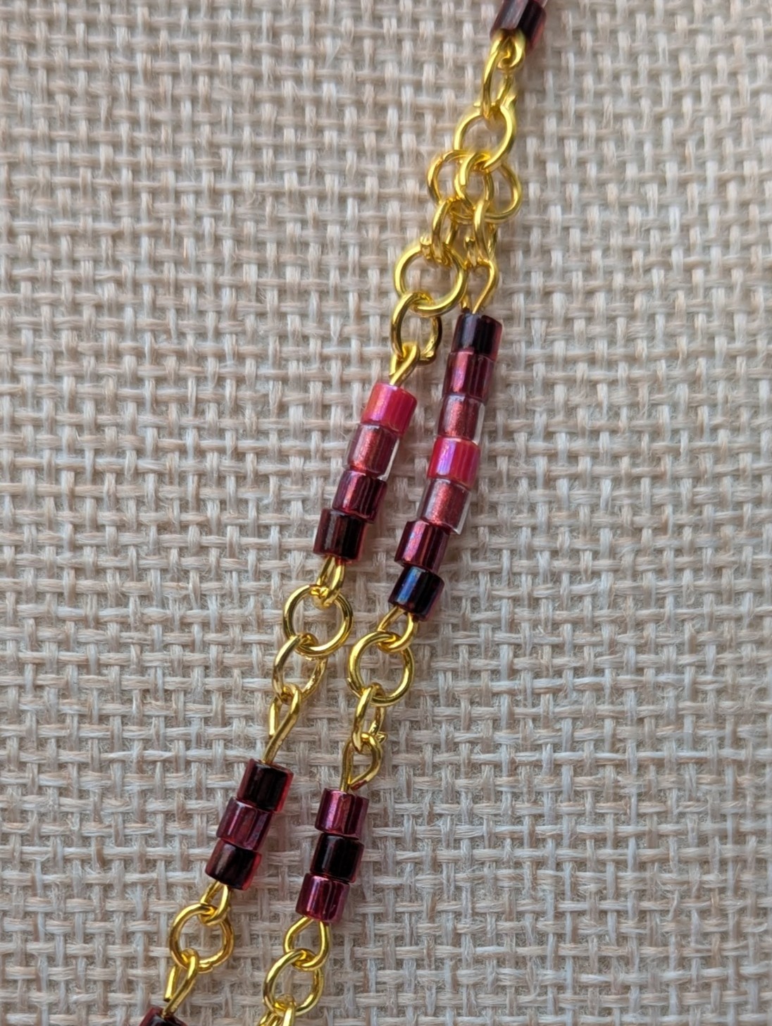 Handmade gold-toned double chain necklace with garnet, burgundy, and deep wine glass seed beads, featuring an ornate gold pendant and lobster clasp closure.