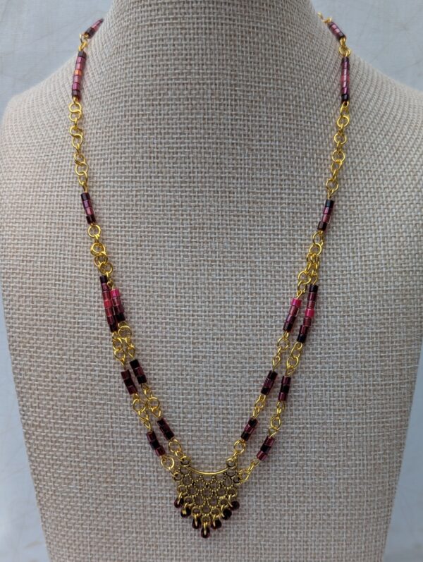 Handmade gold-toned double chain necklace with garnet, burgundy, and deep wine glass seed beads, featuring an ornate gold pendant and lobster clasp closure.