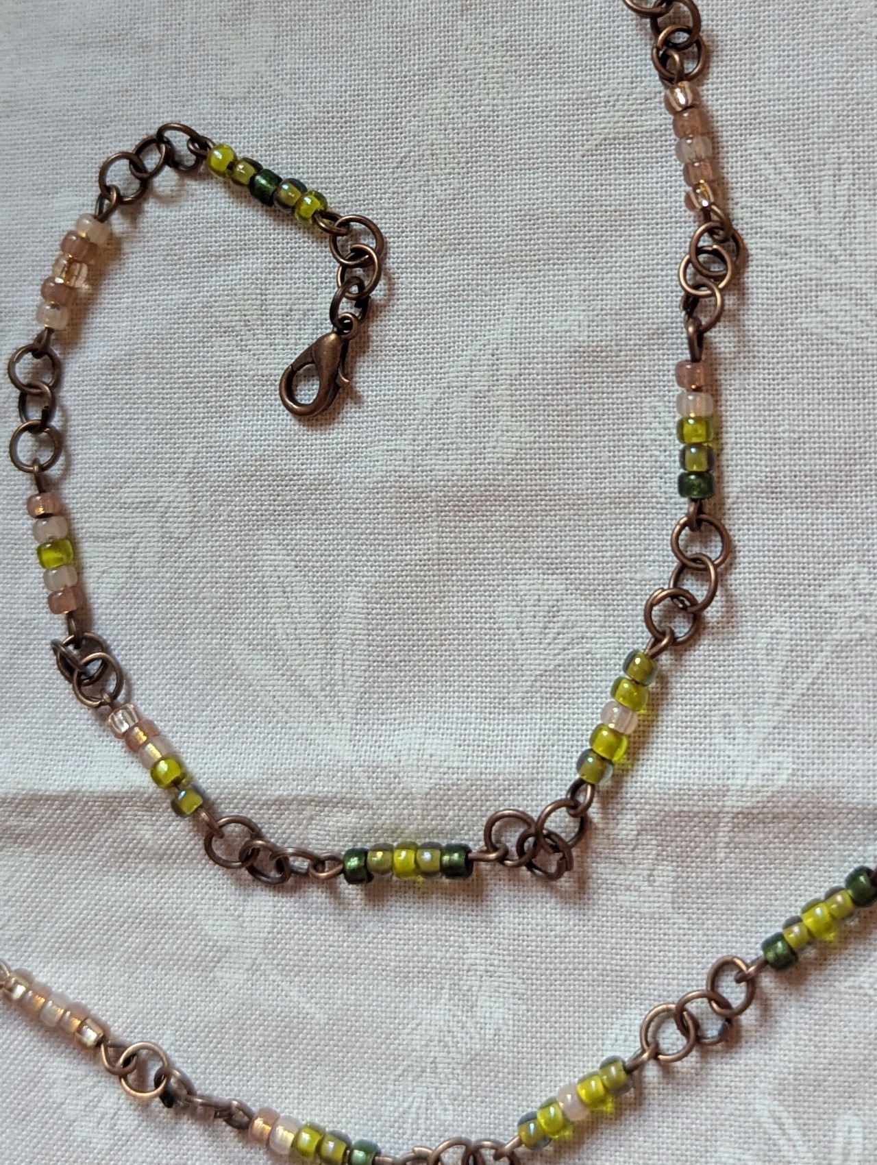 Bronze chain necklace with gradient green glass seed beads in moss, olive, and forest tones with lobster clasp