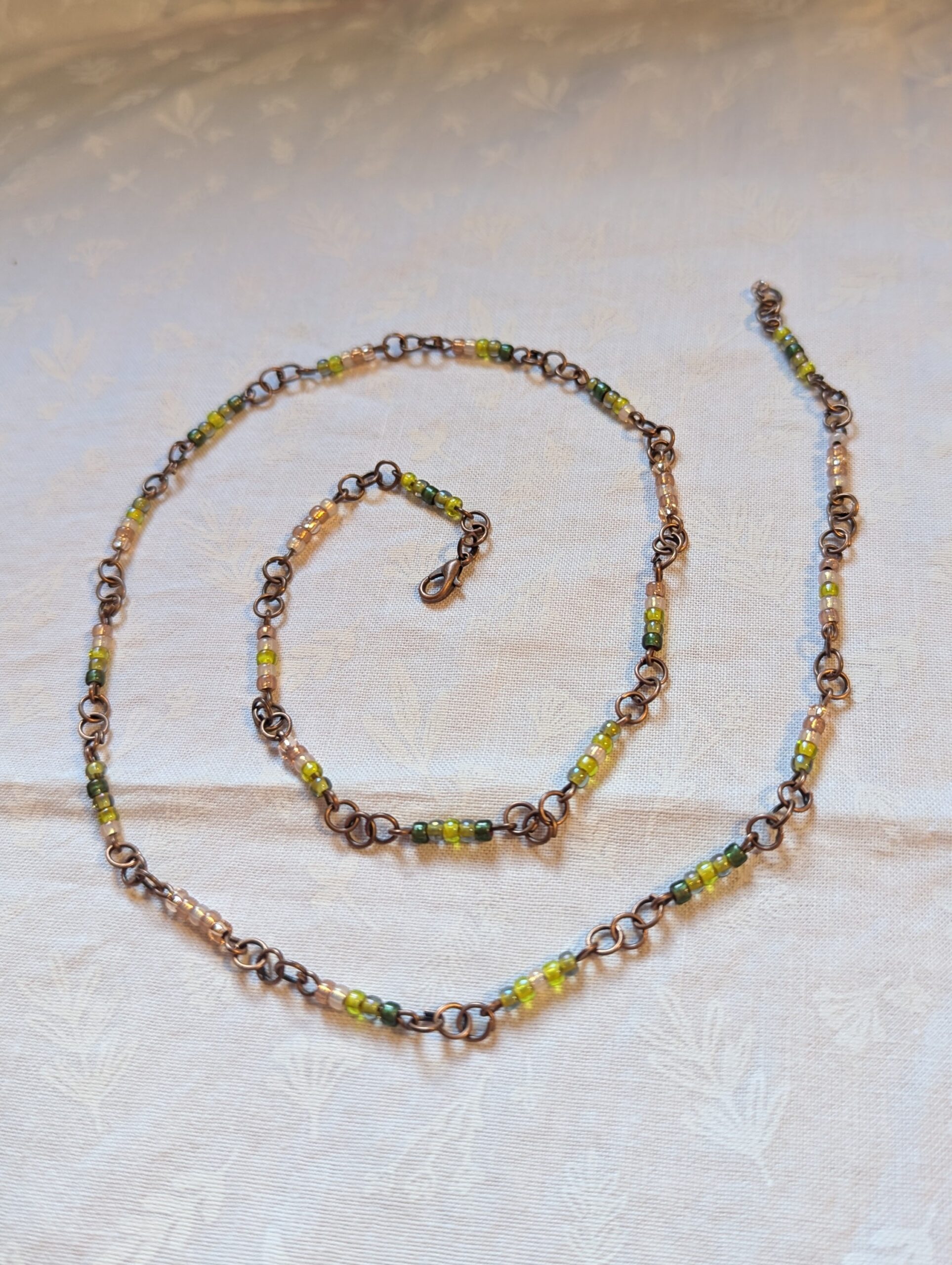 Bronze chain necklace with gradient green glass seed beads in moss, olive, and forest tones with lobster clasp