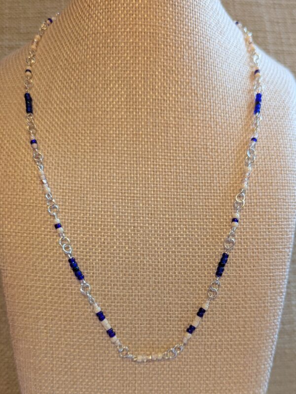 Handmade silver chain necklace with gradient blue and white glass seed beads, displayed on a neutral fabric bust